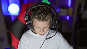 Adorable blond boy streamer, serious face focused on game, playing in dark gaming room with digital tech, sporting headset and sitting at computer table