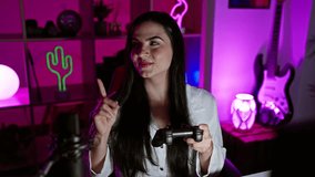 Cheerful young hispanic woman, a joyful gamer, confidently pointing with a smile while playing video game in gaming room at night.