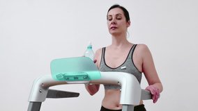 Young woman is exercising on a treadmill and drinking water to hydrate her body, Video Clip 4K