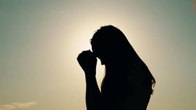 Faith in god. Christian woman praying at sunset close-up. Girl on background of sky in rays of sun prayer to family and children. Relaxation and meditation in nature. Apologize. Hope. Silhouette - Powered by Shutterstock - Get 15% off with code: PIKWIZARD15