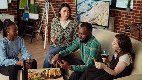 Inclusive group of friends at house party using smartphone to laugh at social media posts made by acquaintance. Amused guests in living room using phone to look at cringe images posted online by mate