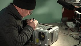 electronics repair. elderly man in a hat in the workshop. soldering of the printed circuit board. High quality video in 4k
