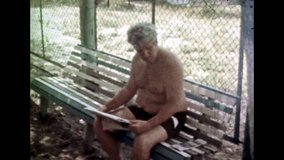 Man in swimsuit read newspaper, woman near beach relax house. Soviet recreation center in summer vacation. People relaxation in sea resort. Vintage color film. Family holiday archive. Retro 1980s