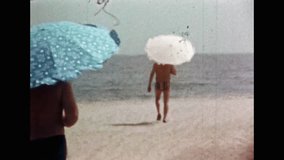 Back view, people walk to relax on sandy beach on blue sea backdrop. Happy holidays on sea coast in sunny, hot summer. Vacation near ocean. Carefree leisure. Vintage color film. Retro archive 1980s
