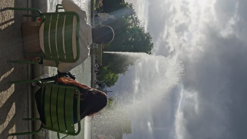Multi-ethnic People Sitting in Front of Fountain at the Jardin des Tuileries. a couple of lovers sits in front of a fountain in Paris, Man and a woman look at the fountain, Slow motion. Vertical view