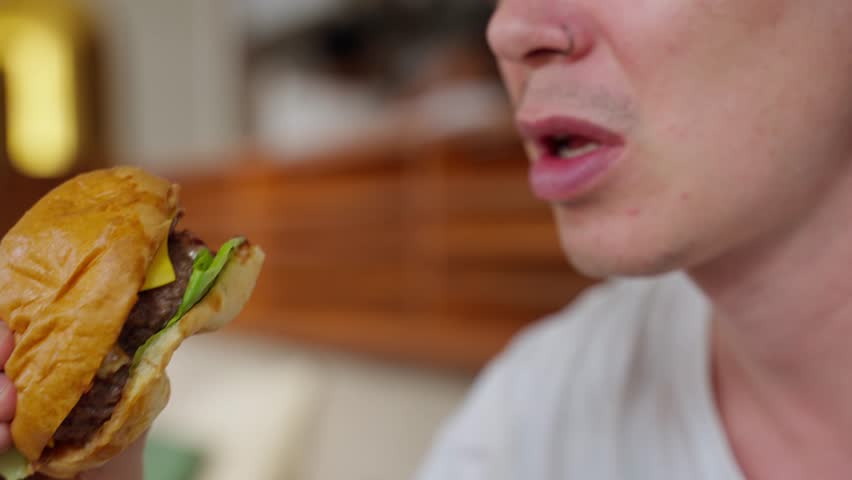 Young Slim Man Eating Unhealthy Food, Burgers, Enjoying Dinner, Eating on the Sofa at Home