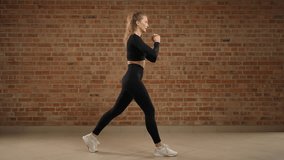 Split squat. Fitness trainer in black sportswear demonstrates the correct execution of the exercise, split squat. She is in an empty hall with a brick wall. Camera 8K RAW. - Powered by Shutterstock - Get 15% off with code: PIKWIZARD15