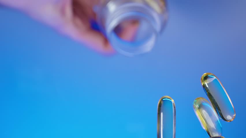 Close up shot hand pouring omega 3 fish oil capsules vitamine D3 vitamin E capsules on flat surface from a plastic transparent bottle