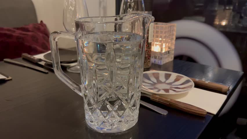 Dining table in the luxury restaurant. Water Jug And Drinking Glass On The Table. Restaurant table with wine glasses and napkins. Romantic dinner place setting with plates and cutlery on table. 