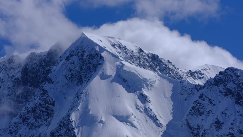 Time lapse of clouds moving across the sky past high snow-capped mountains. 