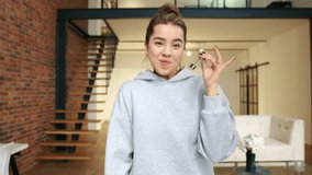 An ecstatic young woman shows off her new house keys, her smile wide with pride and accomplishment, standing in a modern loft. Camera 8K RAW.  - Powered by Shutterstock - Get 15% off with code: PIKWIZARD15