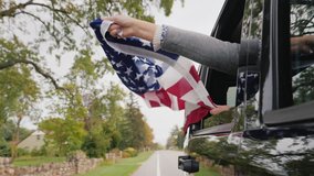 A man holds a large American flag in his hands, pokes him out of the window of a moving car . Slow Motion video