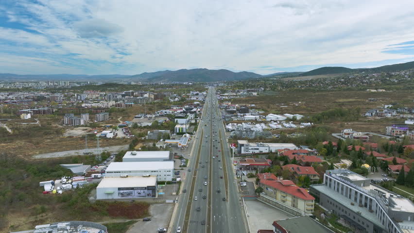 Aerial video, flying over traffic in Sofia, Bulgaria. Broad divided highway encircling the capital (Okolovrasten pat). The urban scenery is in autumn daylight but sun is hidden behind clouds. 