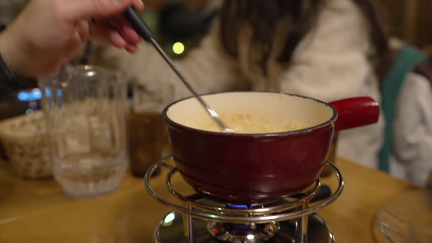 Closeup of fondue at restaurant - tradition Swiss cheese cuisine at diner. Pot underneath heater with fork dipping piece of bread into melted cheese