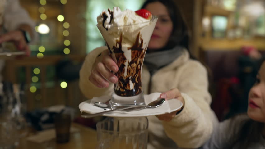 Serving ice cream sundae at restaurant table, children grabbing spoons and eating dessert at diner in the evening, siblings enjoy sugar sugary food with whipped cream Royalty-Free Stock Footage #3415541233