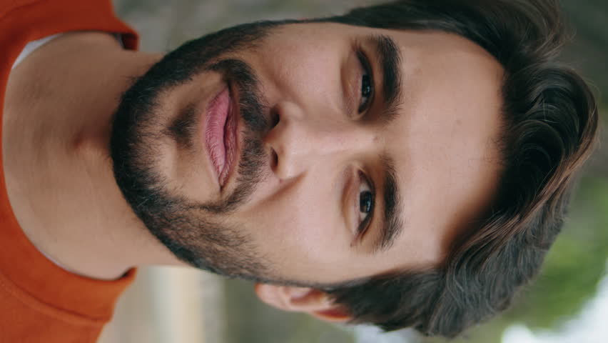 Vertical portrait of happy bearded man looking camera with smile standing forest alone. Handsome young guy posing on green nature close up. Attractive confident hipster relax on weekend outdoors.
