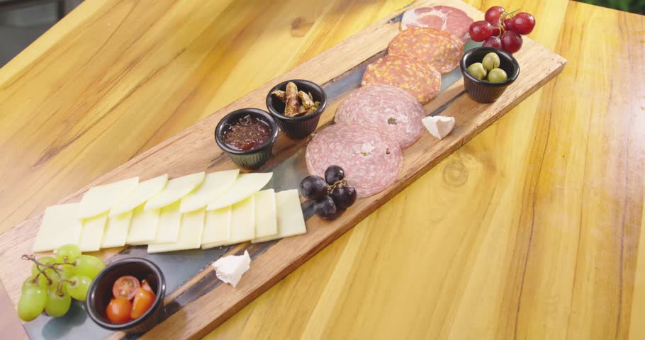 Preparation of a delicious starter of ham, cheese, red grapes, purple grapes, cherry tomato, jelly, fresh olives. Delicious board of hams and cheeses with fruit to share at a table gourmet party