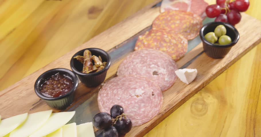 Preparation of a delicious starter of ham, cheese, red grapes, purple grapes, cherry tomato, jelly, fresh olives. Delicious board of hams and cheeses with fruit to share at a table gourmet party