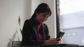 Confident Asian businesswoman, at her modern office-style desk, is actively typing and chatting with her friend on her smartphone.  - Powered by Shutterstock - Get 15% off with code: PIKWIZARD15