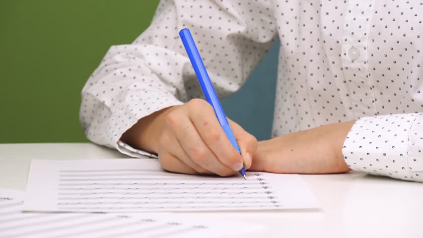 A child writes with a pen while sitting at a desk with a speckled plan. A schoolboy studying notes, music school, music children