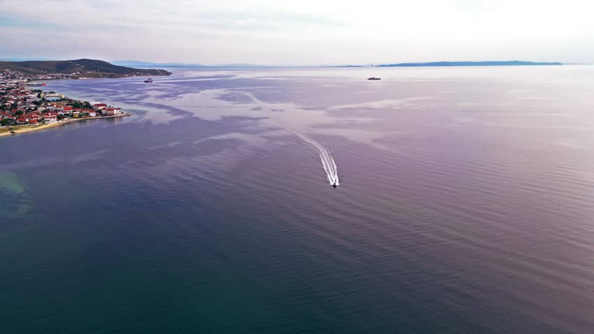 Nature captures: a boat moving swiftly in the sea water under a cloudy sky, taken by a drone.
Type: aerial view
Direction: forward
