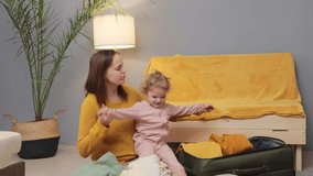 Toddler-friendly journey. Mom's travel care. Adventure-packed suitcase. Caucasian woman packing suitcase for trip with baby daughter on floor in living room at home - Powered by Shutterstock - Get 15% off with code: PIKWIZARD15