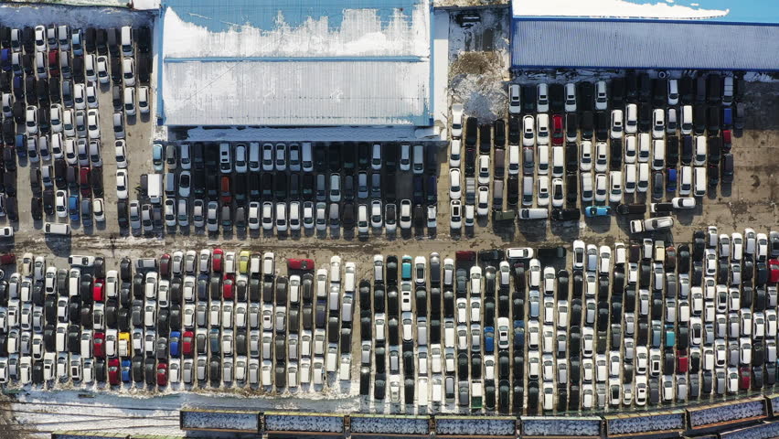 Aerial: a parking lot with rows of cars from top to bottom at customs in Vladivostok awaiting paperwork. A tow truck with a car drives through a parking lot