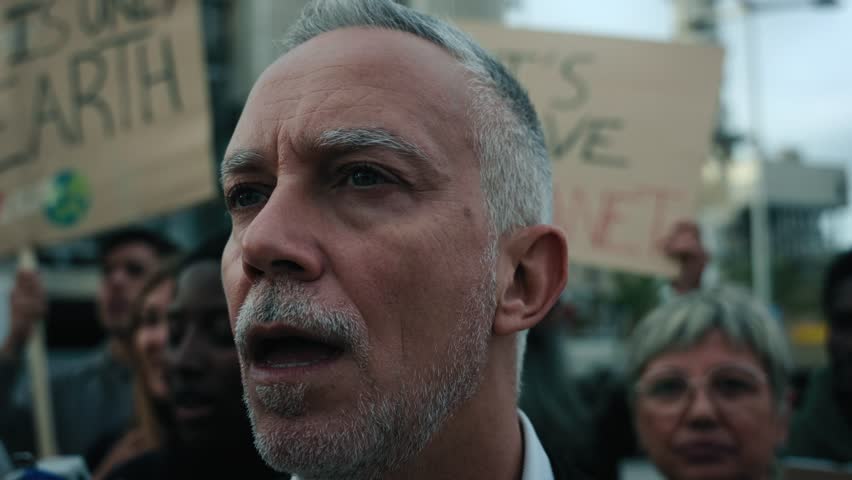 Close up Angry and rebellious mature man shouting and protesting with megaphone at demonstration at climate change and global warming. Group of activists pro-earth people manifestation with banners Royalty-Free Stock Footage #3416203721