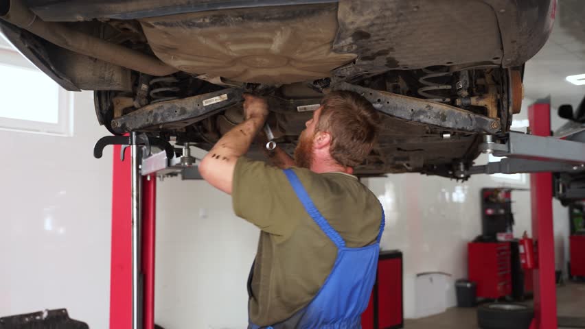 Auto mechanic fixes vehicle suspension. Expert examines, adjusts car undercarriage, conducts maintenance, utilizes tools in garage. Workshop repair, professional service, maintenance guide visual.