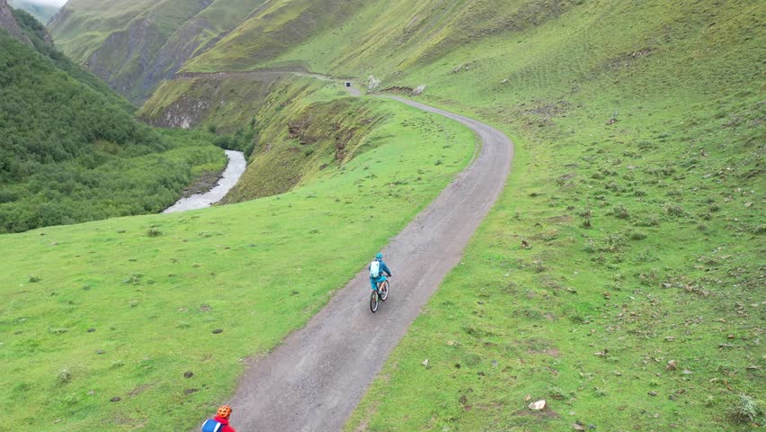 A drone footage of two persons cycling on an unpaved mountain trail on a cloudy day in Georgia
