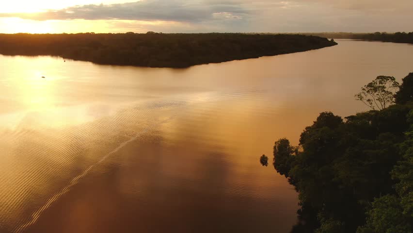 Aerial view of amazing sunset above of Amazon river. Drone flight of beautiful red yellow sunset clouds and sky. Jungle trees background. Vacation time journey with boat trip. 4K wide angle