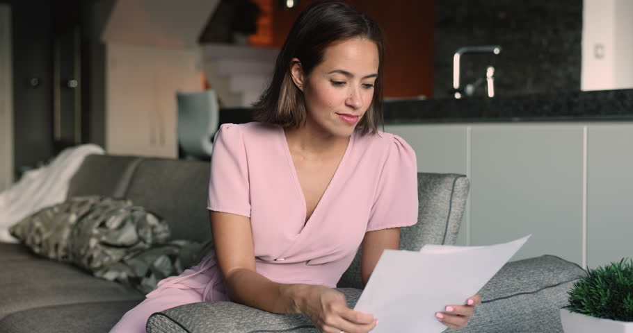 Focused young 30s Caucasian woman sit on couch at home read postal paper letter, get message from bank, receive written notice of loan repayment, learn business correspondence, consider legal document Royalty-Free Stock Footage #3416459979