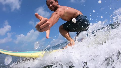 Surfer rides crystal clear ocean wave at sunny day and shows the Shaka sign
