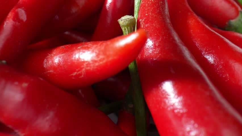 Explore the graceful intricacies of red chili peppers, as they shimmer and glisten in macro view, unveiling the secrets of their spicy allure with every frame. Fruit and vegetable concept. 4K HDR.