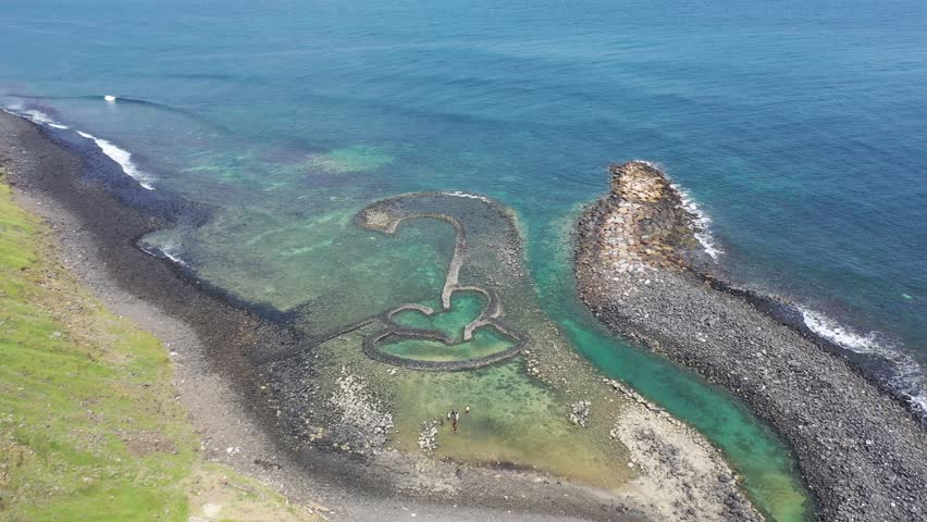 Aerial view of the beautiful Double-Heart of Stacked Stones or Twin-Heart Fish Trap, which is an old traditional fishing weir by the coastal cliffs of a cape, in Cimei Isalnd, Penghu, Taiwan Royalty-Free Stock Footage #3416607965