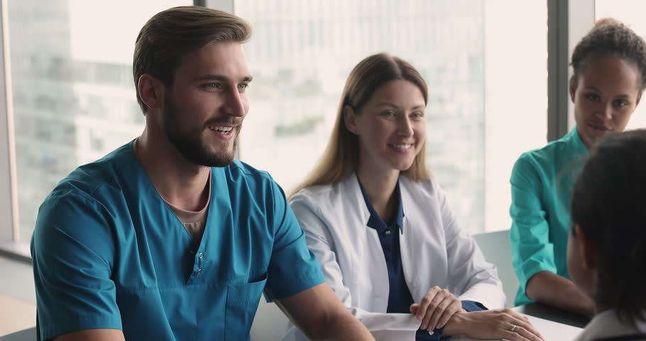 Handsome young doctor man in blue uniform speaking to multiethnic colleagues at meeting table, discussing job in hospital, medical profession, giving surgeon expertise, consultation Royalty-Free Stock Footage #3416651591