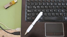 The man working in his office with the computer, placing the memory stick and taking notes with the white pen, forms an original video clip with a black keyboard background