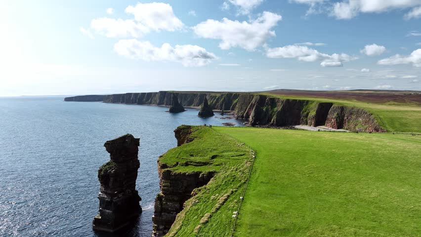 A drone flight over a green meadow with a viewpoint of the Duncansby Stacks. North Coast 500 route in the north of Scotland.