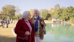Video of a mature couple chatting and walking along an urban park with an artificial pool