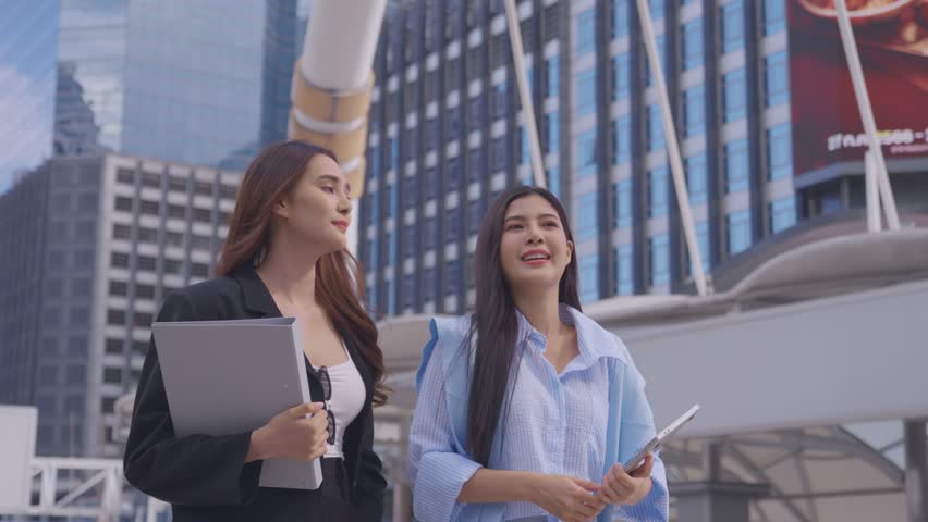 Asian two businesswoman walking with confidence outdoors in the city. Attractive beautiful female employee worker people feel happy and relax while spend leisure time walk outside to office company.