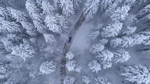 Aerial - Top down tracking shot of blue car drifting on snowy road in forest