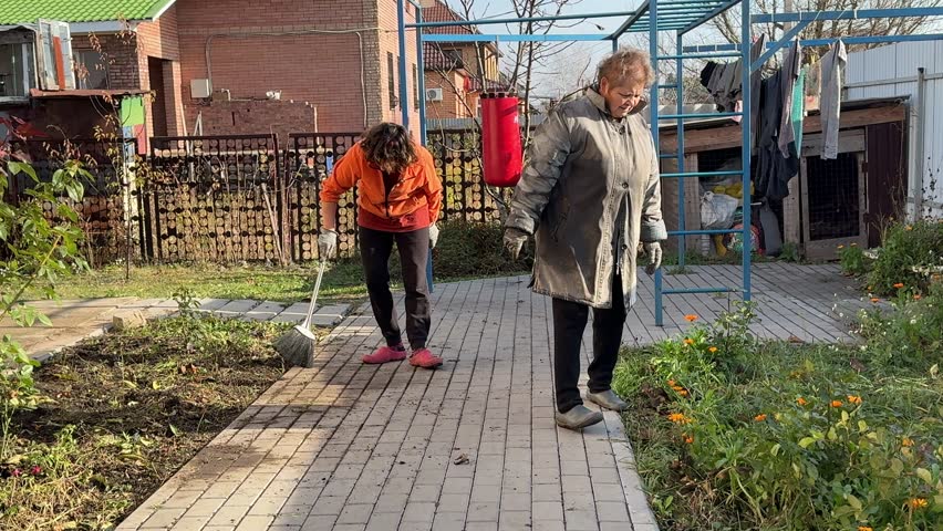 Women clean the sidewalk near the house.