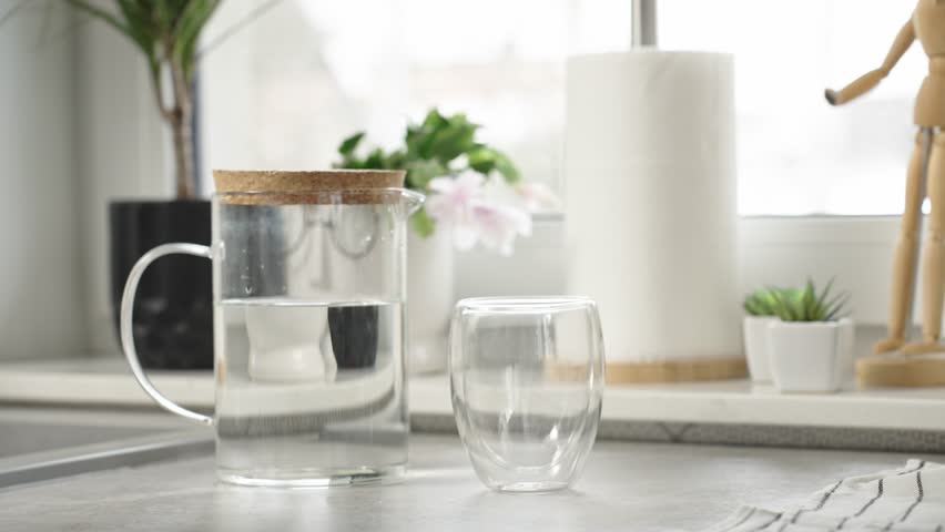 Woman pouring fresh pure water from jug into glass in kitchen, Quenching thirst, Lifestyle healthcare concept