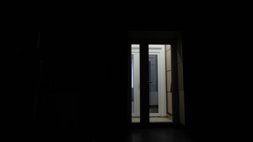 View through the backlit glass doors a man enters a dark room. A man's silhouette opens the door and enters a room with the lights off. Backlight. copy space for the inscription. Royalty-Free Stock Footage #3417091433
