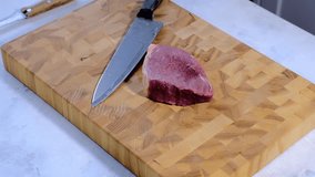 A woman in a plaid shirt cuts meat into slices for preparing stew on a wooden board. Video recipes, cooking