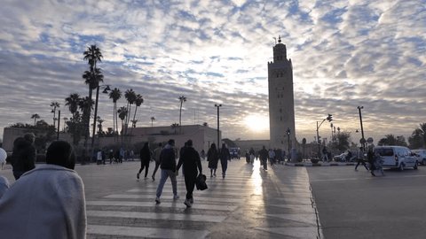 Marrakech, Morocco - 2 Jan 2024: Pedestrians cross the street by using crosswalk lines, and vehicles wait during the red light in front of the Kutubiyya Mosque. Redaksjonell arkivvideo