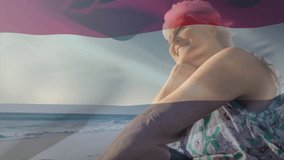 Animation of flag of the netherlands over senior caucasian woman on beach. Patriotism, flags and lifestyle concept digitally generated video.