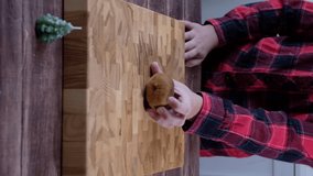A boy in a checkered red shirt cuts a kiwi in half on a wooden board. Video recipes. Children cooking