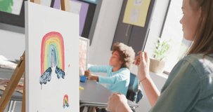 Video of happy caucasian schoolgirl standing at easel painting in art class, copy space. Education, childhood, creativity, inclusivity, elementary school and learning concept.