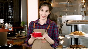 Medium shot Asian barista waitress worker female wearing apron in cafe restaurant holding red cup of hot coffee to camera happy smiling, small business entrepreneur create video clip content promotion
